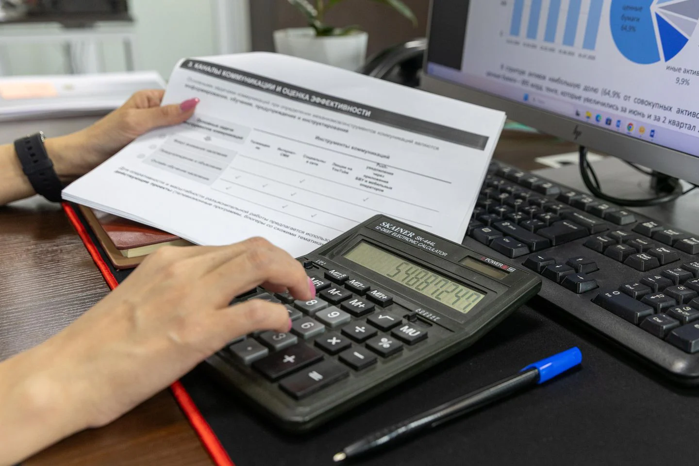Mão usando uma calculadora junto a um documento financeiro sobre a mesa